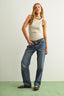 Woman wearing a beige tank top and blue jeans against a plain background