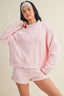 Person wearing a pink sweatshirt and shorts set on a beige background