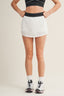 Person wearing a white tennis skirt and black sports top on a beige background