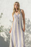 Woman wearing a long, striped dress against a white wall with greenery.