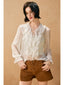 Woman wearing a white blouse with floral details and brown shorts against a beige background