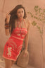 Woman wearing a red dress with white patterns against a beige wall.