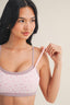 Woman wearing a light pink bralette with a subtle pattern on a plain background