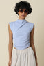 Woman wearing a light blue sleeveless top and white pants against a beige background