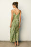 Woman wearing a green and white patterned dress against a white wall.