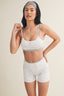 Woman wearing a white sports bra and gray shorts on a beige background