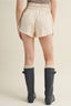 Person wearing cream shorts and black rain boots on a beige background