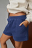 Person wearing blue shorts and a light-colored sweatshirt on a gray background