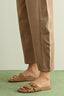 Brown sandals worn with brown pants on a green surface
