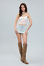 Woman wearing a white lace top, light blue denim skirt, and brown knee-high boots on a gray background
