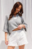 Woman wearing a textured gray top and white skirt against a plain background