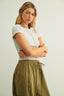 Woman wearing a white top and green skirt against a plain background