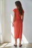 Woman wearing a red dress standing in a bright room with sunlight filtering through curtains.