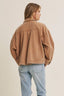 Person wearing a brown jacket and light blue jeans on a plain background