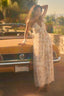 Woman in a long dress standing next to a vintage car with a blurred background