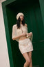 Woman in a white outfit standing against a green door