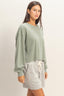 Woman wearing a green oversized sweatshirt and gray shorts on a plain background