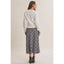 A woman is shown from the back wearing a cream crewneck sweater and a navy and gray plaid midi skirt, paired with black high-heeled sandals, against a solid light beige studio background.