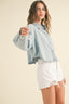 Woman wearing a light blue denim jacket and white shorts on a beige background