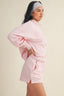Woman wearing a pink sweatshirt and shorts set with a beige background
