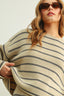 Woman wearing a beige sweater with black stripes and sunglasses on a plain background