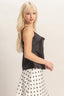 Woman wearing a black sleeveless top and polka dot skirt on a plain background