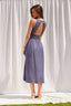 Woman wearing a purple dress with an open back against a white curtain background