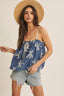 Woman wearing a blue top with white patterns and denim shorts on a beige background