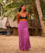 Woman in a black top and purple skirt standing on a sandy beach with palm trees in the background