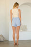 Woman wearing a light-colored sleeveless top and blue shorts in a minimalistic room.