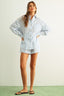 Woman wearing a light blue striped shirt and shorts against a white background