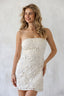 Woman wearing a white strapless lace dress against a plain background