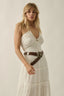 Woman wearing a white dress with a brown belt against a plain background