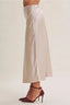 A model is shown from the waist down wearing a high-waisted, wide-leg satin midi skirt in a light champagne beige color, paired with dark burgundy ankle-strap heels, against a solid light beige studio background.