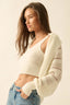 Woman wearing a cream-colored cardigan over a white top with blue jeans on a beige background