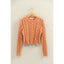 Orange cable knit sweater on a hanger against a beige wall