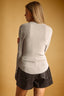 A woman shown from the back wearing a light beige ribbed knit long-sleeve top and dark brown shorts, set against a solid warm tan background.