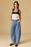 Woman wearing a black and beige crop top with blue jeans on a beige background