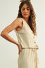 Woman wearing a beige sleeveless top and pants with sunglasses on her head against a white background