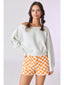 Woman wearing a light gray sweater and orange checkered shorts on a white background