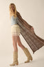Woman wearing a long brown patterned shawl over her shoulders with a neutral background