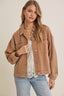 Woman wearing a brown jacket over a white top and blue jeans on a beige background