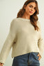 Woman wearing a beige knitted sweater and blue jeans against a plain background