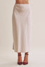 A model wearing a light beige or cream-colored midi skirt with a side slit, paired with dark red high-heeled sandals, shown from the waist down against a plain light beige background.