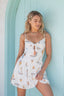 Woman wearing a white dress with sailboat pattern against a light blue wall.