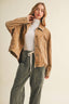 A woman modeling a light brown corduroy jacket over a white turtleneck and dark green wide-leg pants, set against a plain beige studio background.