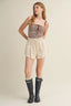 Woman wearing a striped tank top, beige shorts, and black rain boots on a plain background