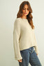Woman wearing a beige knitted sweater and blue jeans on a plain background