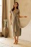 Woman wearing a gray wrap dress standing in a room with a vase and plant.