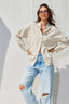 Woman wearing a beige striped button down shirt and light blue jeans against a white wall
